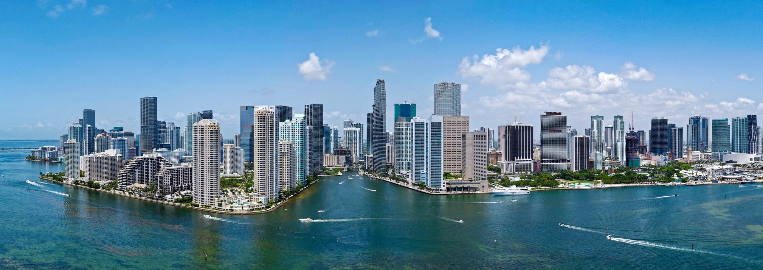 Wide aerial panorama of the Brickell skyline seen across Biscayne Bay, with Brickell Key in the foreground