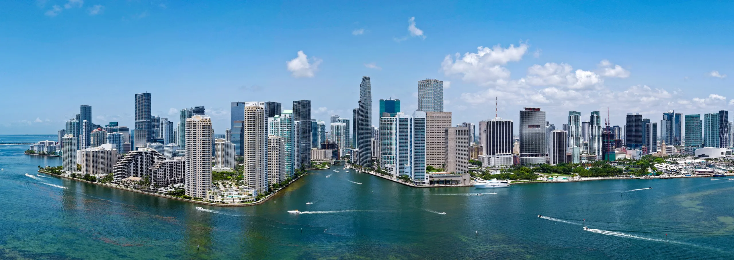 Wide aerial panorama of the Brickell skyline seen across Biscayne Bay, with Brickell Key in the foreground
