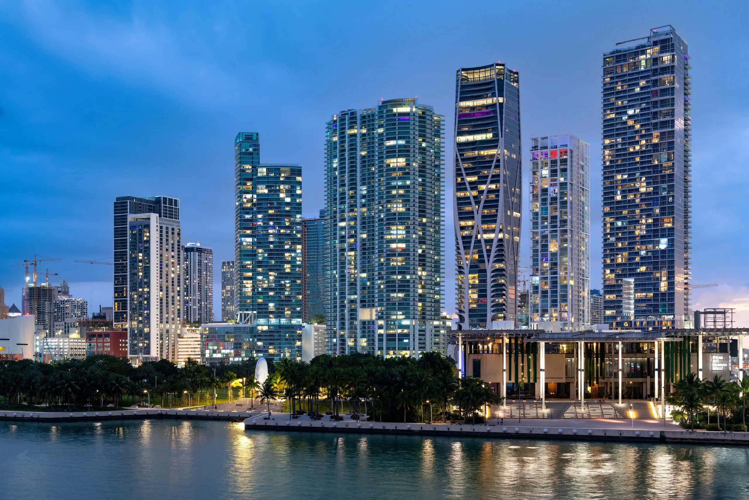 Downtown Miami towers at dusk seen across the water, with Maurice A. Ferré Park along the bayfront