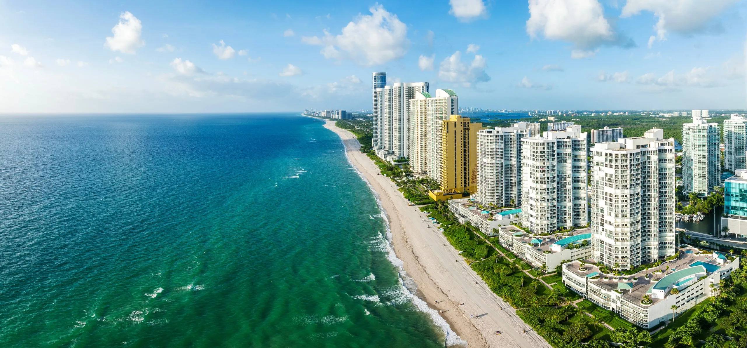 Aerial view north along the Sunny Isles Beach shoreline, towers and pool decks set back from the sand